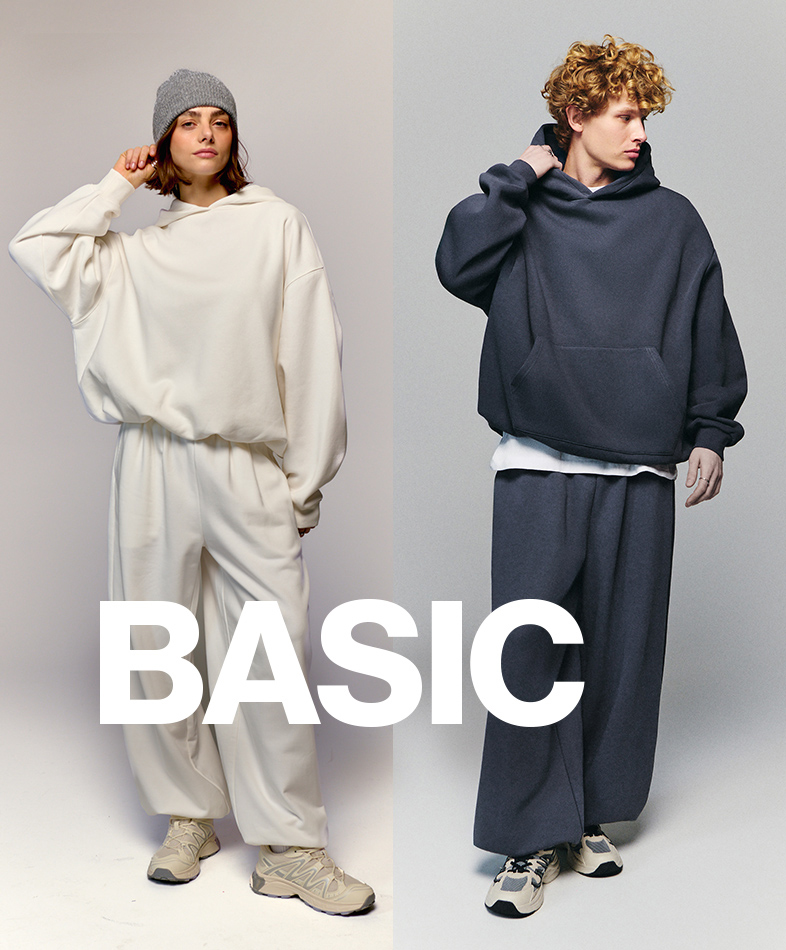 Two people are shown wearing loose, casual outfits consisting of hoodies and wide-leg pants. The image highlights a minimalist, comfortable style. The word "BASIC" is prominently displayed in bold, white font across the image.
